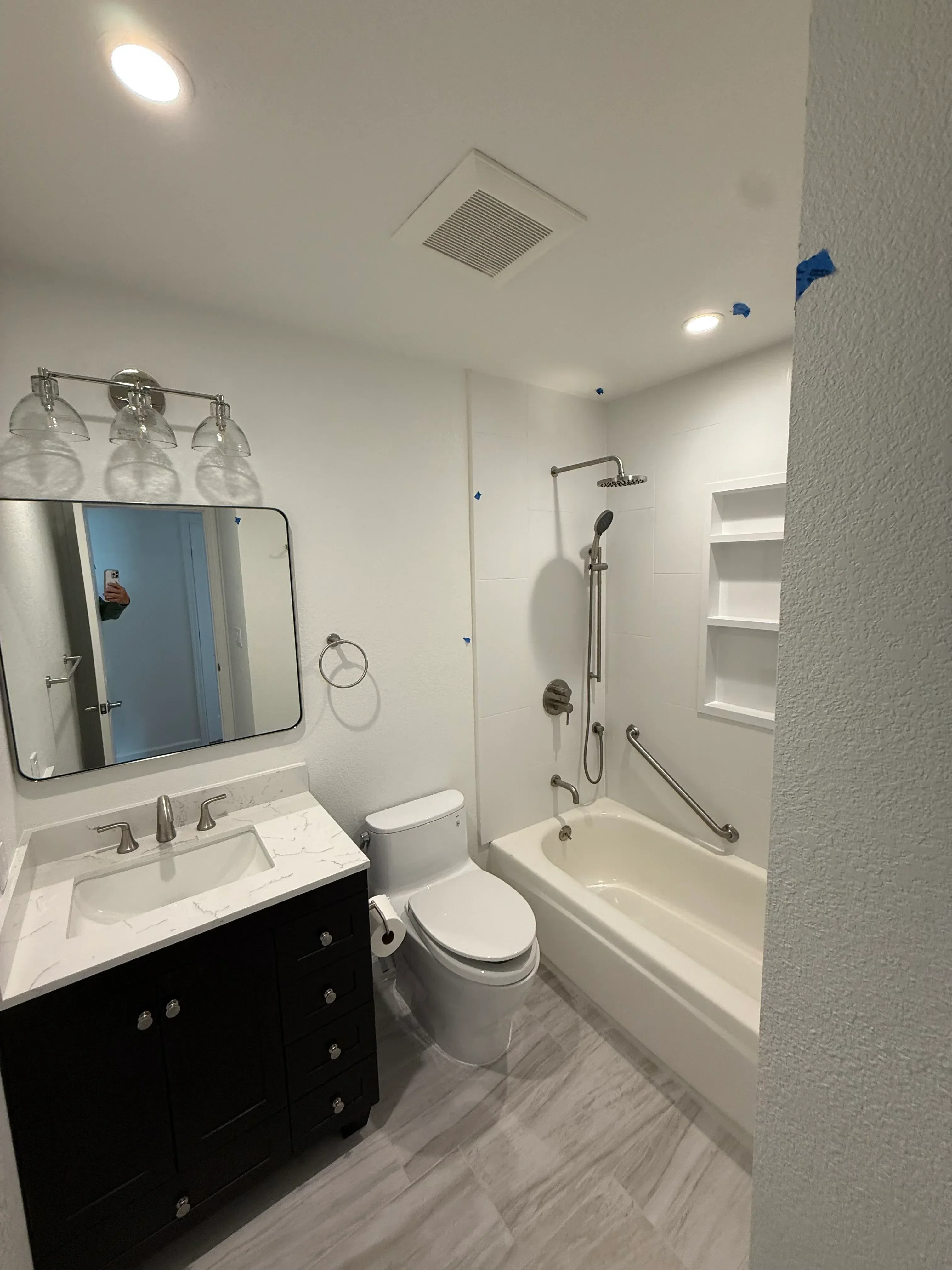 Newly renovated bathroom with white drywall, recessed lights, chrome fixtures, and tiled shower surround