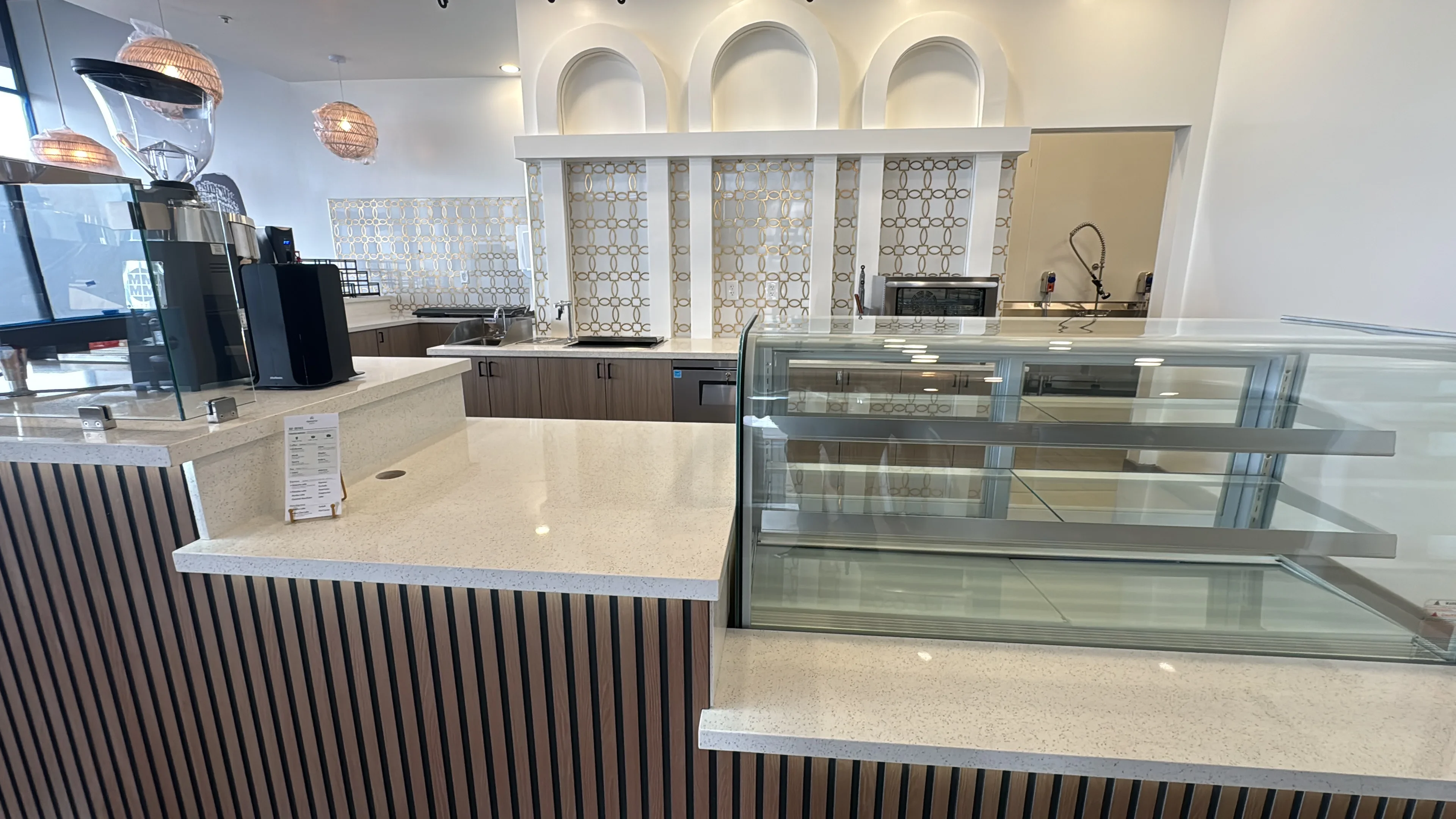 Commercial bakery counter with fluted wood cabinetry, quartz top, and refrigerated glass display case