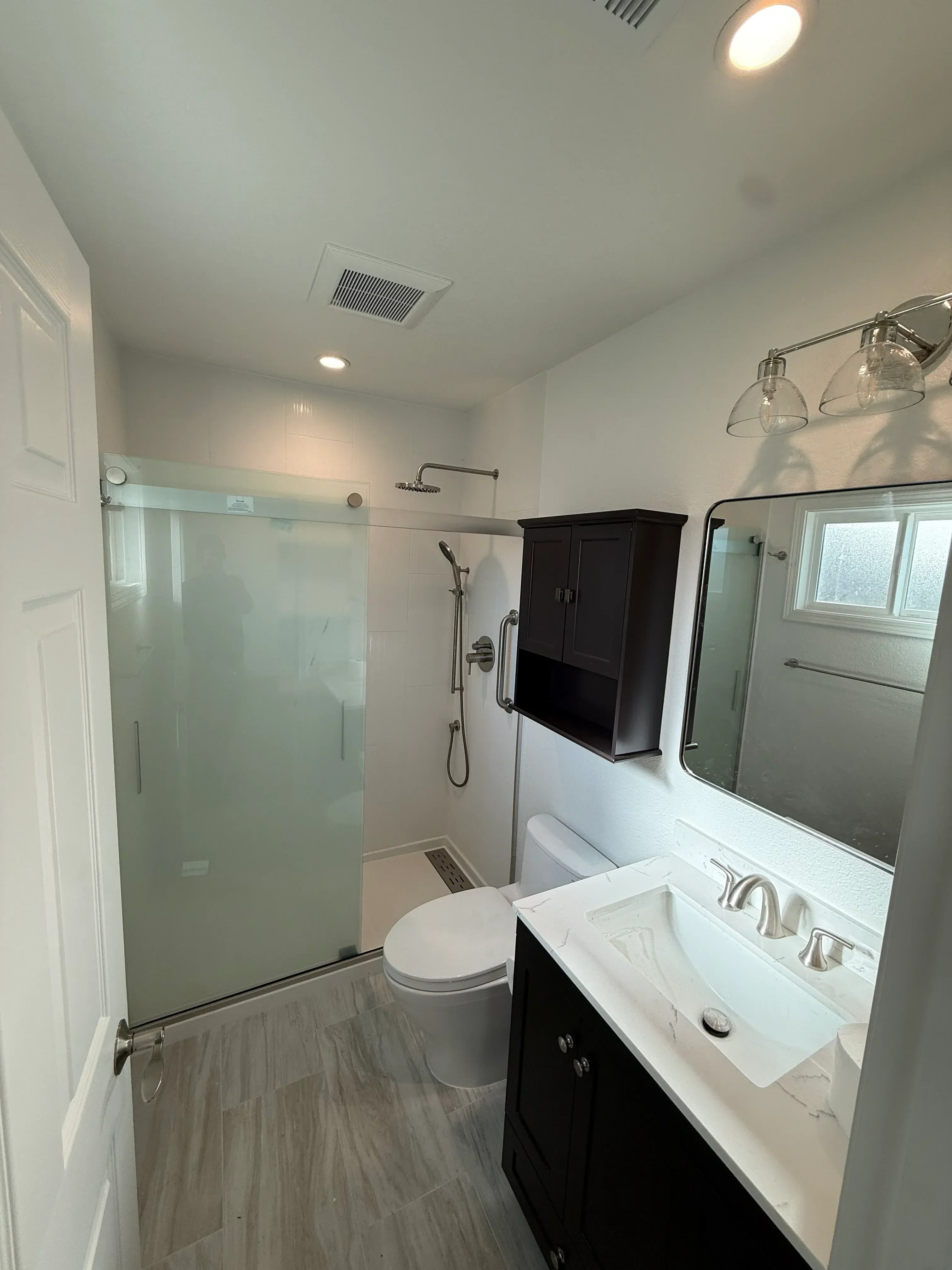Bathroom with frameless glass shower, white walls, chrome fixtures, and wood-look tile flooring