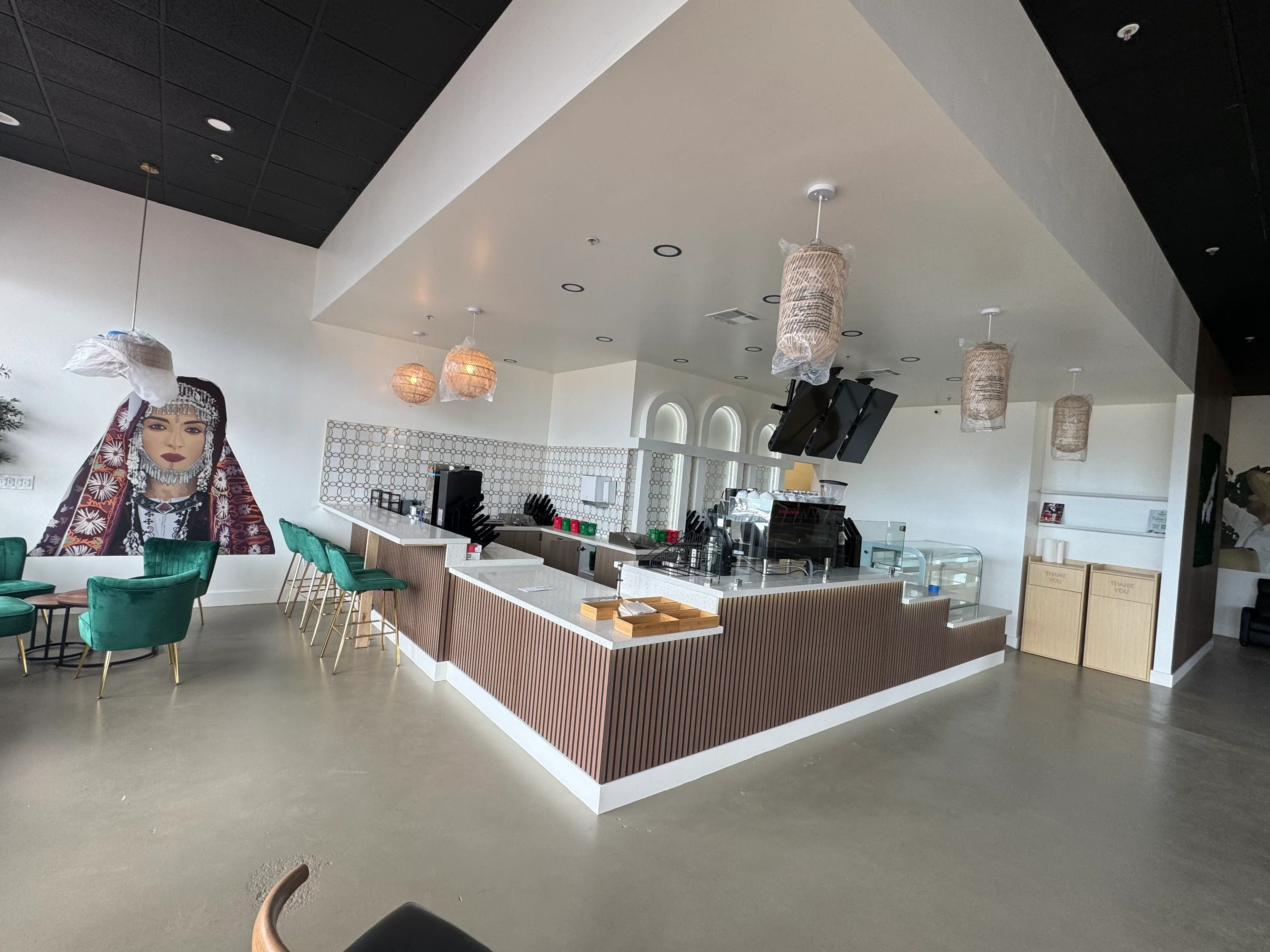 Modern café interior with corrugated metal counter, recessed lighting, pendant fixtures, and polished concrete floors