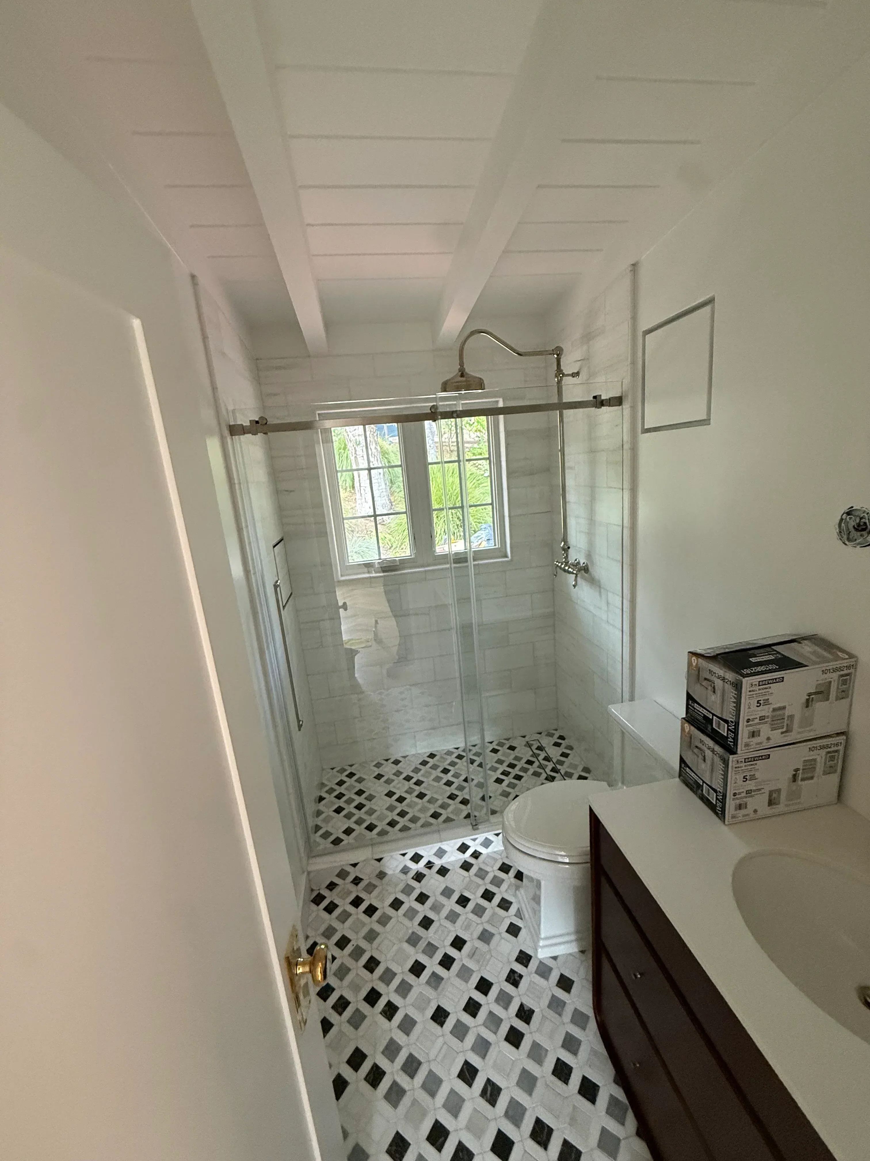 Frameless glass shower enclosure with geometric mosaic tile accent wall and subway tile surround