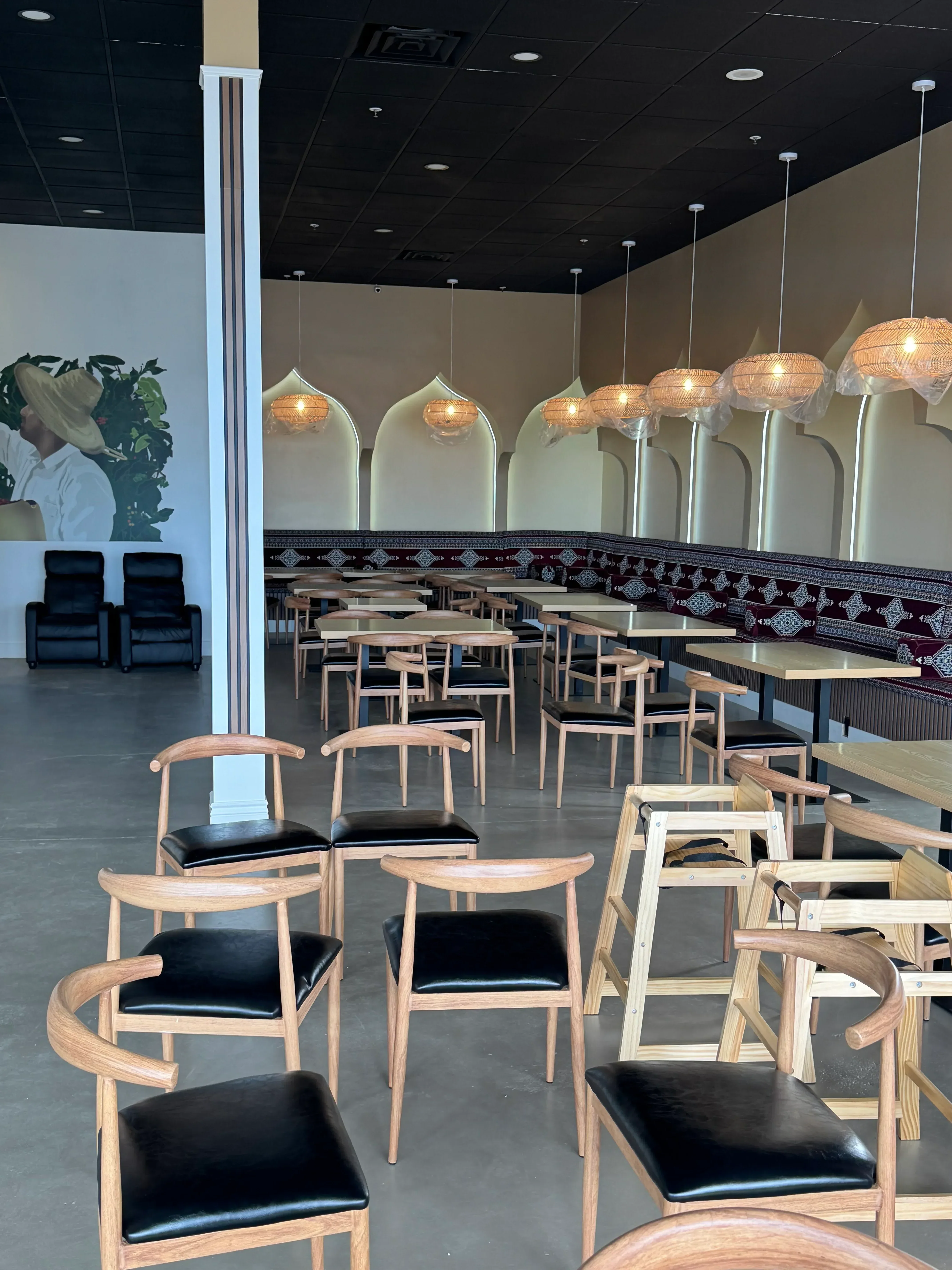 Restaurant dining room with wood chairs, woven pendant lights, black accent wall, and concrete flooring