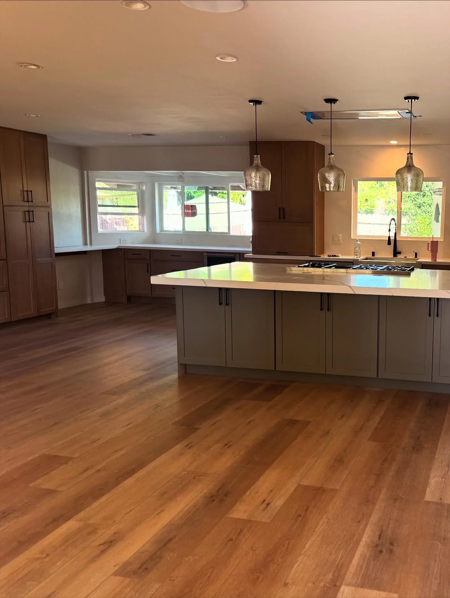 Modern kitchen with wood cabinetry, quartz island countertop, pendant lights, and hardwood floors