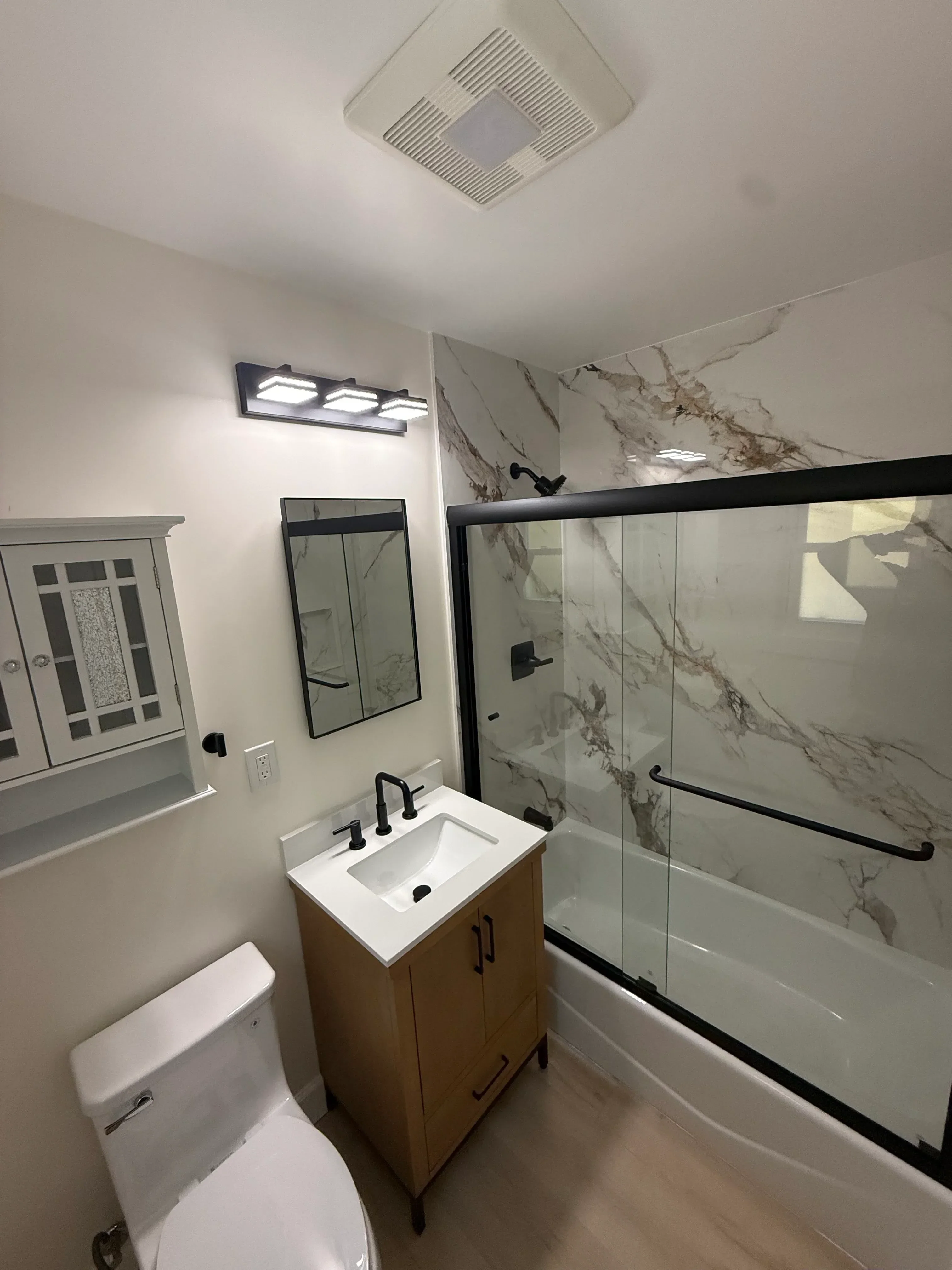 Bathroom with marble tile shower, glass enclosure, white vanity, and matte black fixtures